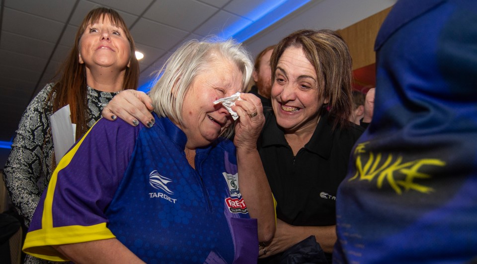 A woman cries while being comforted by another woman at a darts tournament.