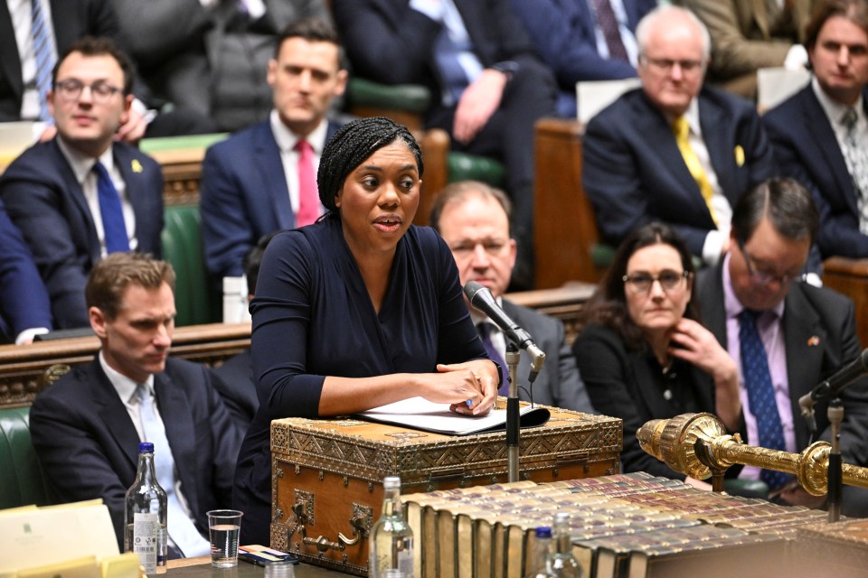 A woman speaks at a podium flanked by two men in suits.