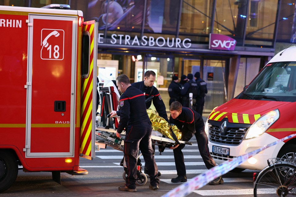 Firefighters loading an injured person onto a stretcher outside Strasbourg train station after a tram collision.