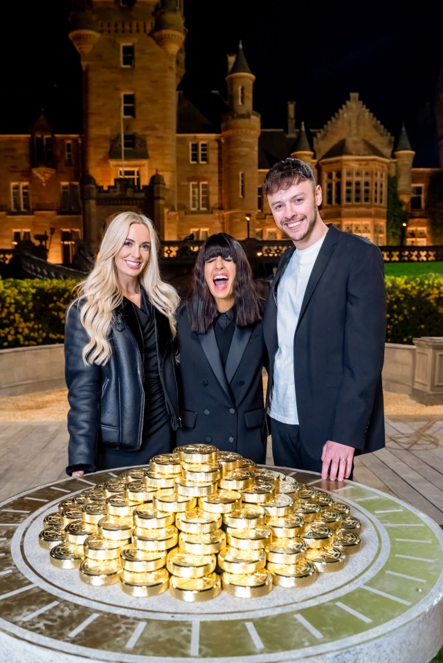 Three presenters stand behind a large pile of gold coins in front of a castle.