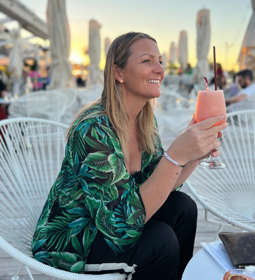 Woman in tropical-print shirt enjoying a pink cocktail outdoors.