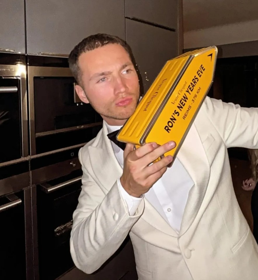 Man in a white tuxedo holding a yellow Ron's New Year's Eve box.