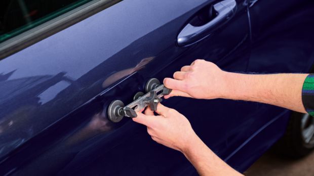 Person using a tool to repair a dent in a car door.