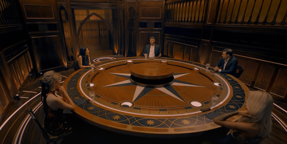 Five people seated around a large, ornate circular table.