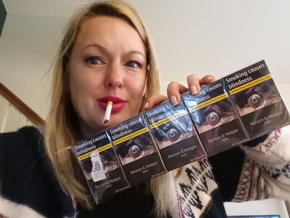 Woman holding several packs of Benson & Hedges Gold cigarettes; each pack shows a graphic warning: "Smoking causes blindness".