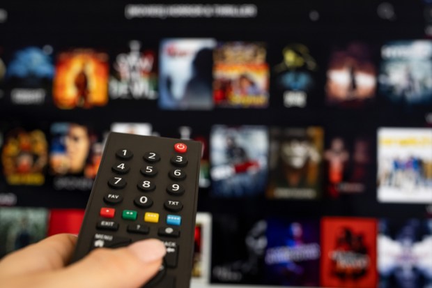 Hand holding TV remote in front of streaming service screen.