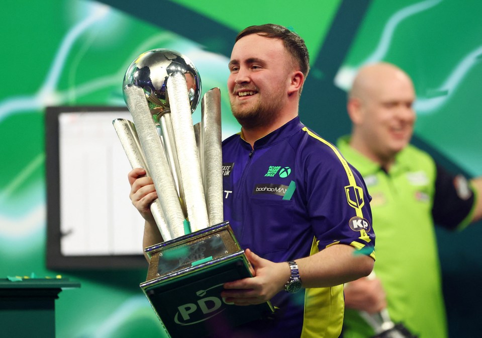 Luke Littler holding the Sid Waddell trophy after winning the PDC World Darts Championship.