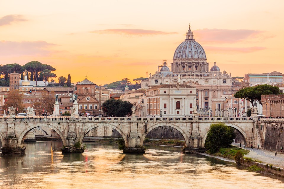 Sunset view of St. Peter's Basilica in Rome, with a bridge over the Tiber River.