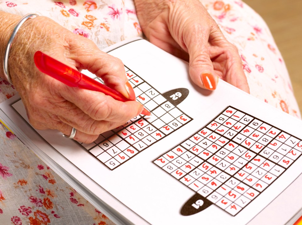 A senior woman's hands solving a Sudoku puzzle.