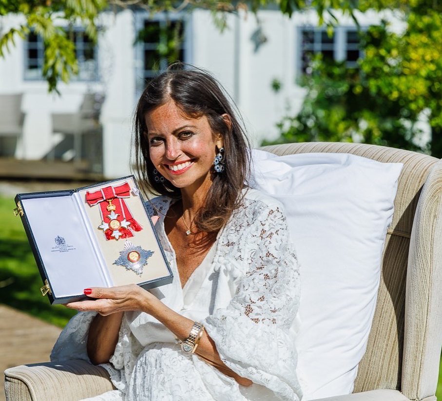 Woman in a white lace dress holding a Damehood award.