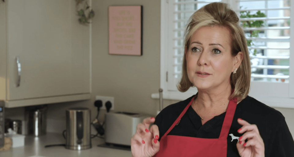 A woman in a red apron talks to the camera.