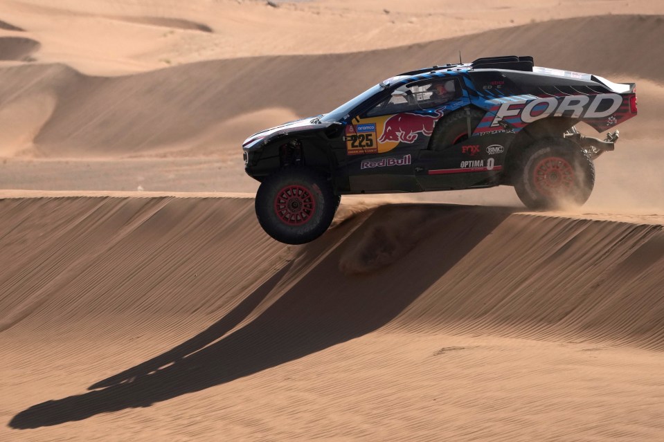 Carlos Sainz and his co-driver navigating a sand dune in a rally car during the Dakar Rally.