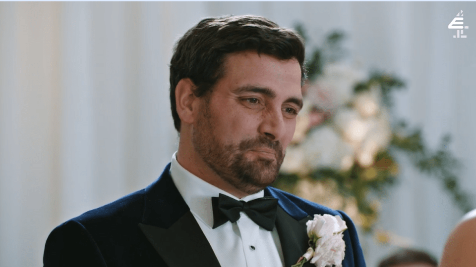 A groom in a tuxedo looks somber at his wedding.