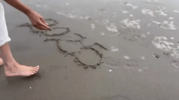 Person drawing hearts in the sand.
