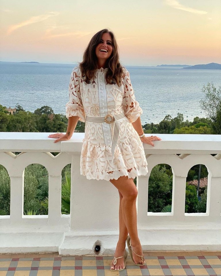 Woman in white lace dress on balcony overlooking ocean.