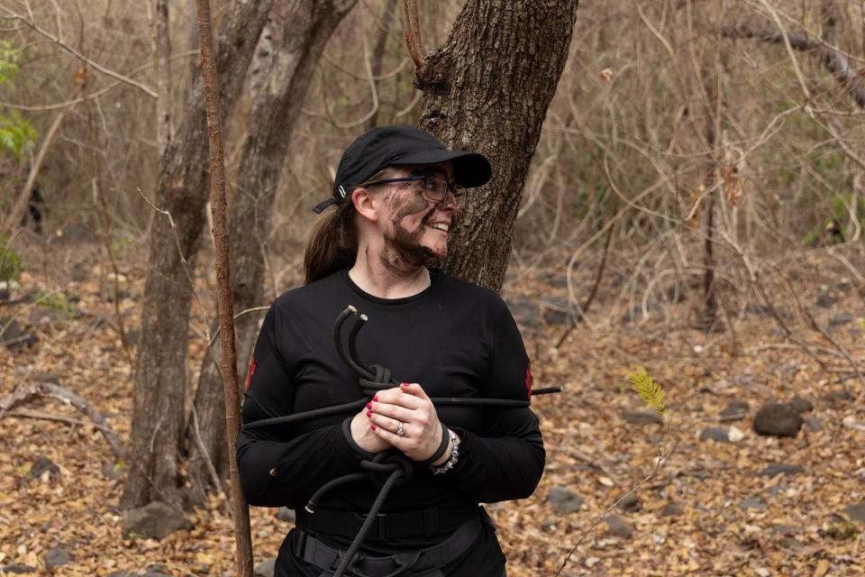 Woman with mud on her face holding rope in a forest.