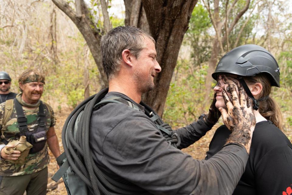 Bear Grylls wiping mud off a woman's face.