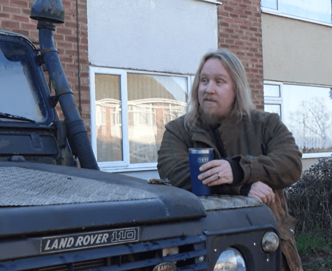 Man standing by a Land Rover Defender, holding a Yeti cup.