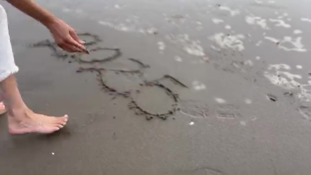 Meghan Markle drawing in the sand on a beach.