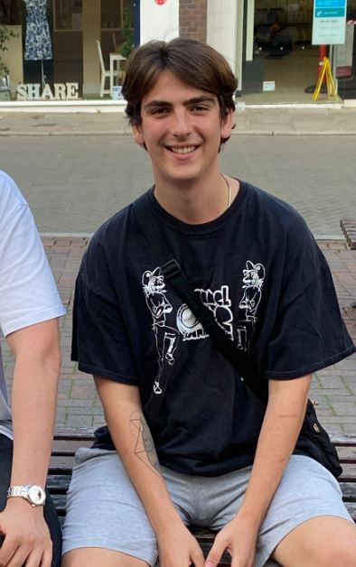 Young man sitting on a bench wearing a black t-shirt and grey shorts.
