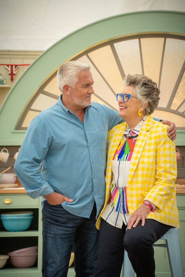 Paul Hollywood and Prue Leith, judges from the Great British Bake Off, stand together in a kitchen.