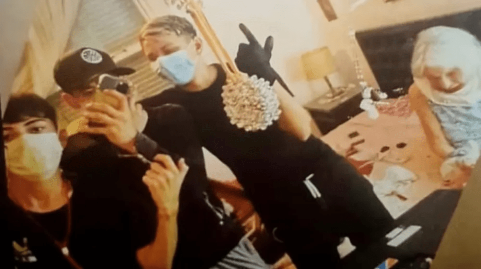 Photo of three masked teens taking a selfie with a distressed elderly woman tied to a bed.