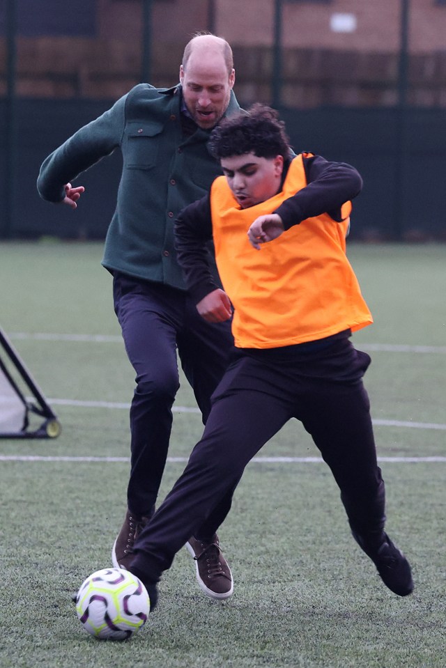 Prince William playing soccer with a young person.