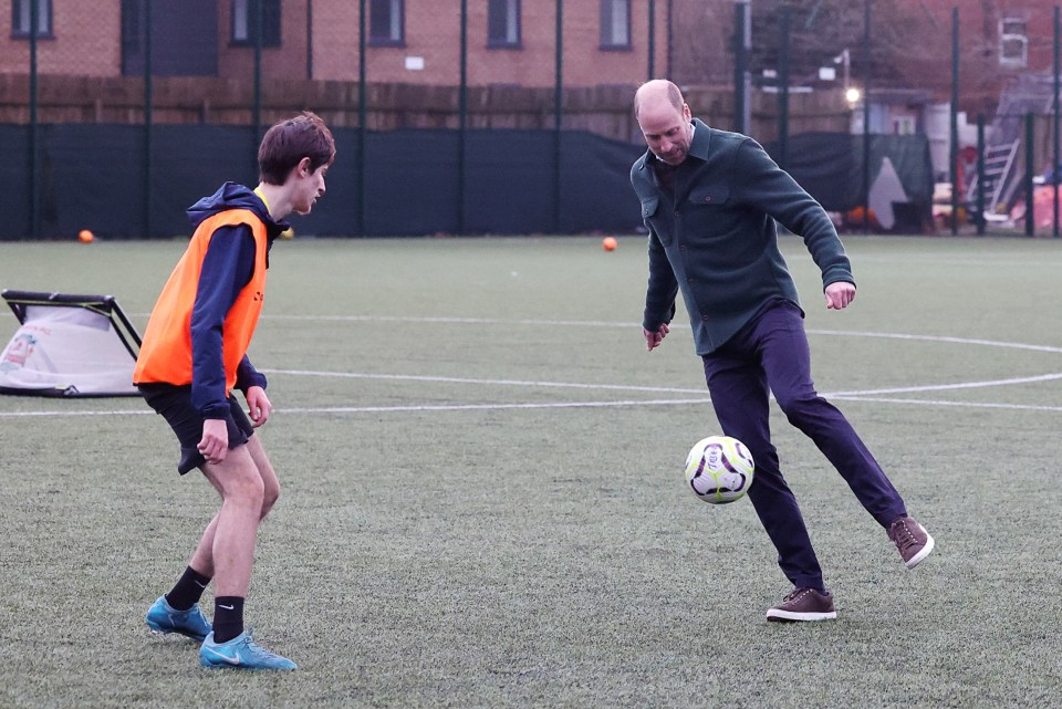 Prince William juggling a soccer ball with a young person on a playing field.