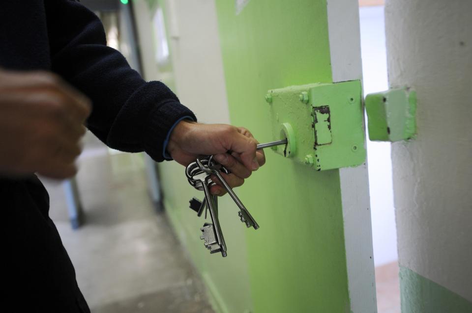 A prison warden unlocks a cell door.