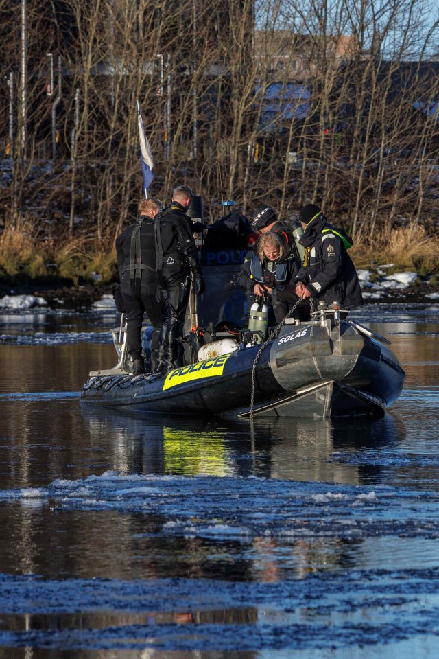 Police divers searching a river from a boat.
