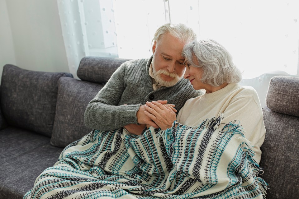 Senior couple cuddling on a couch under a blanket.