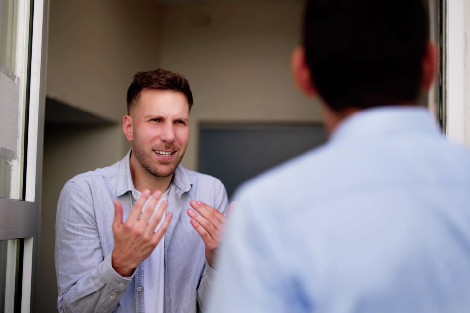 A young man angrily argues with his neighbor at his doorway.