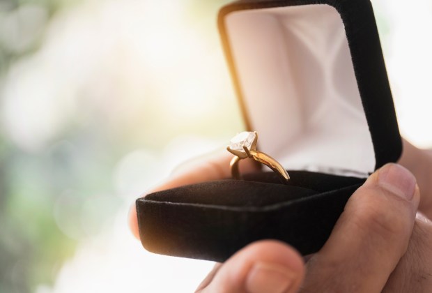 A hand holding an open ring box with a diamond engagement ring.