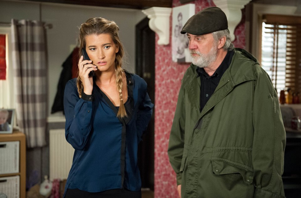 A woman on a phone call, looking concerned, stands next to a man in a green jacket.