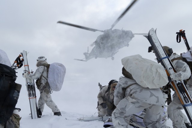 US and Finnish special forces soldiers on skis approach a helicopter in snowy arctic conditions.