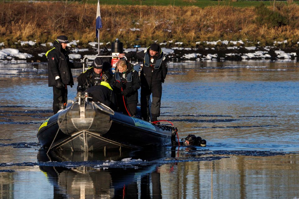 Police divers searching a river from a boat.