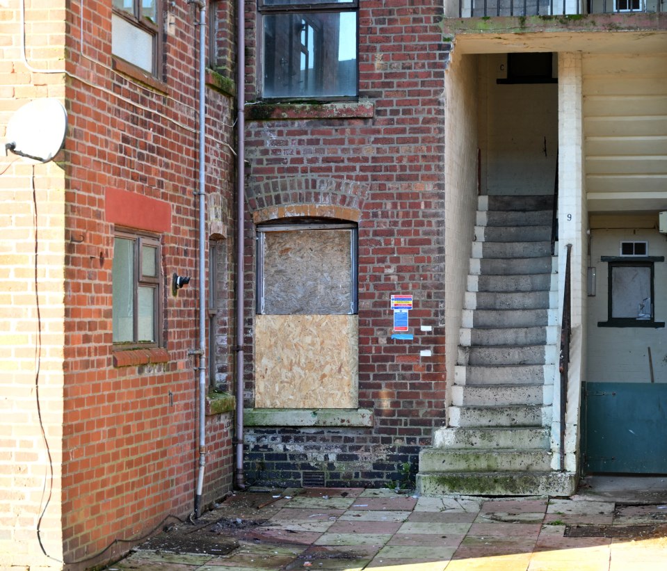 Boarded-up window and exterior stairs of a brick building.