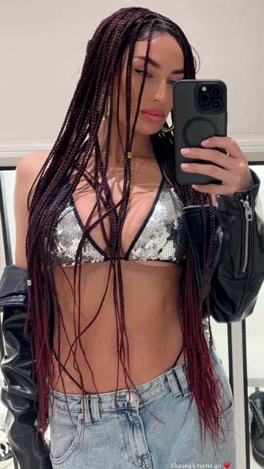 Woman with long braids taking a selfie in a silver sequined bikini top and jeans.
