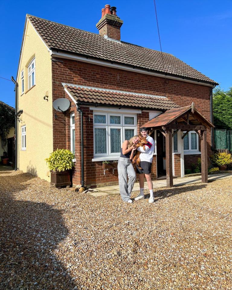 Couple standing in front of their new house with their dog.