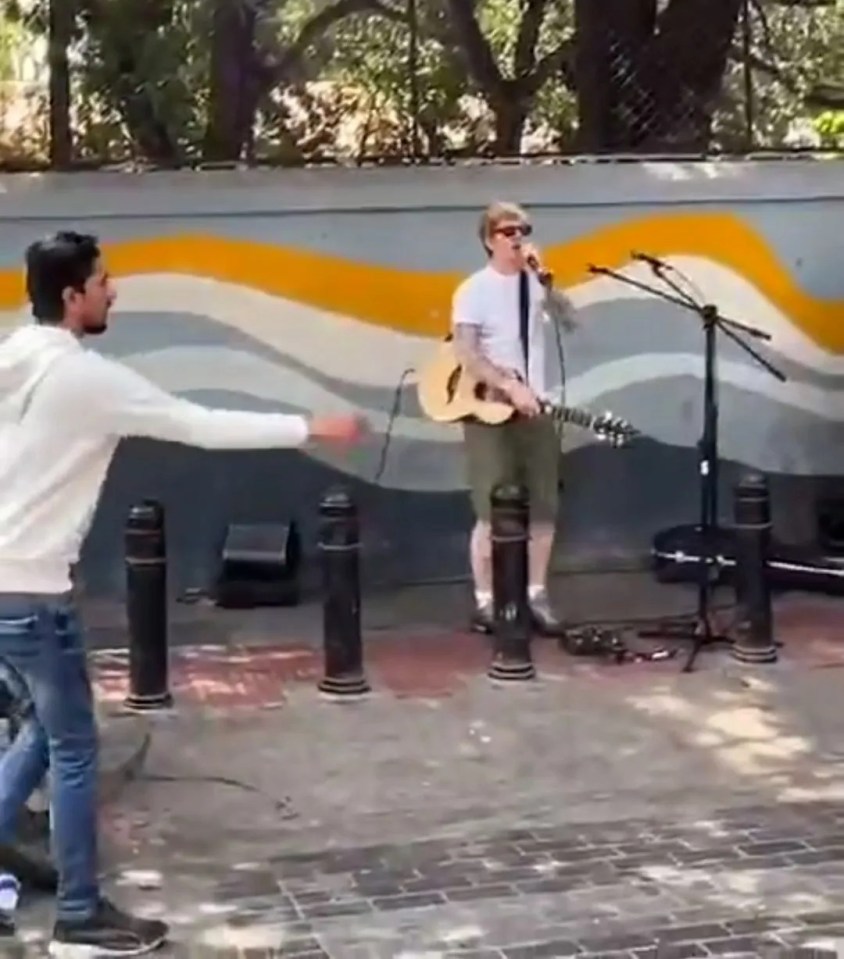 Ed Sheeran busking on a street in Bangalore, India, having his microphone unplugged by a police officer.