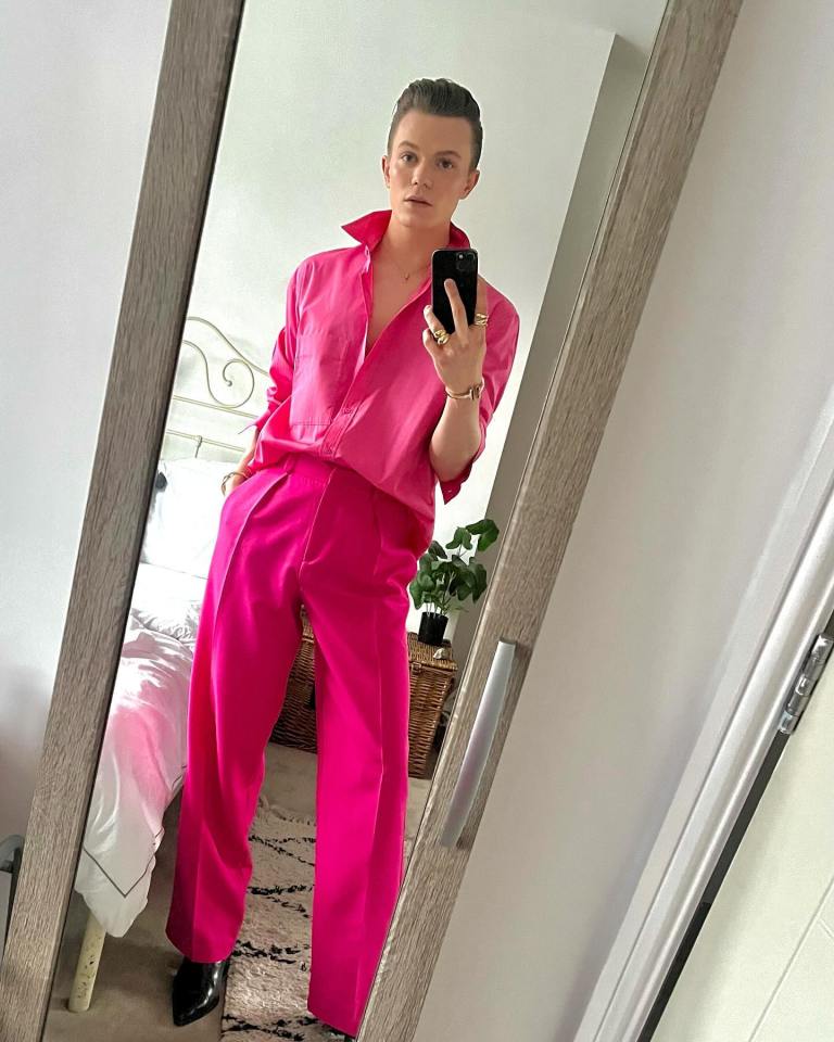Man in a bright pink shirt and pants taking a selfie in a mirror.
