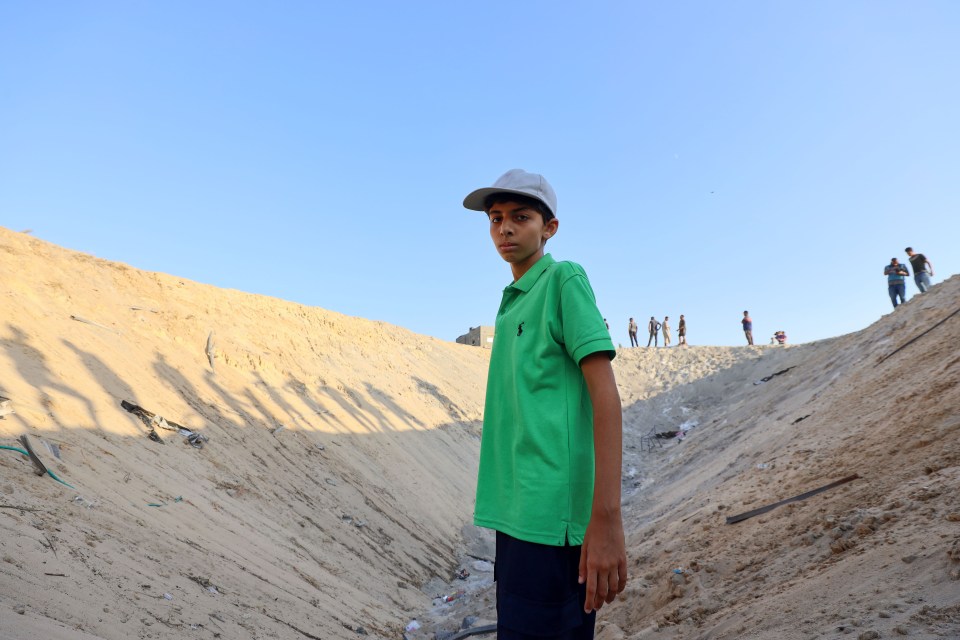 Boy in green shirt standing in bomb crater.