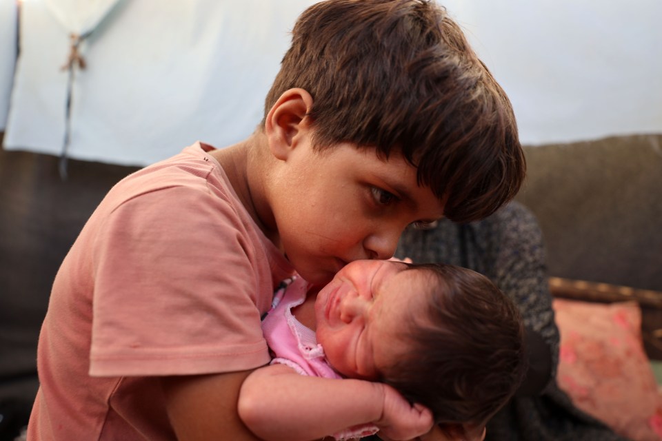 A boy gently kisses a baby.