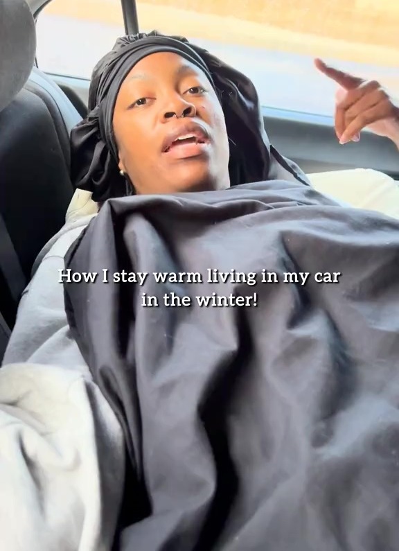 Person wrapped in blankets in a car, explaining how they stay warm during winter.