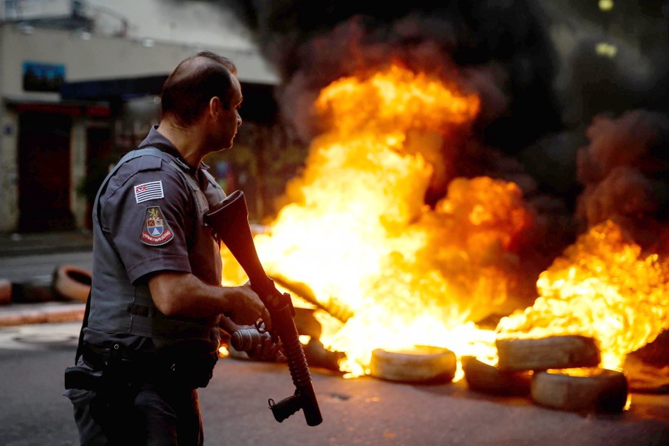 Police officer at a protest with burning tires.