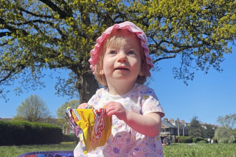 Toddler outdoors holding a snack.