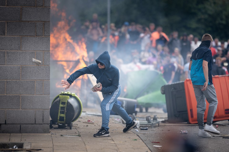 A hooded person throws a rock during a riot.