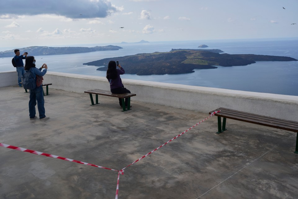 Tourists taking photos of Santorini island with emergency crews deployed due to seismic activity.
