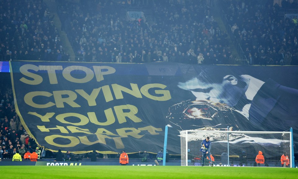 Manchester City fans displaying a banner that reads "Stop Crying Your Heart Out" at a soccer match.