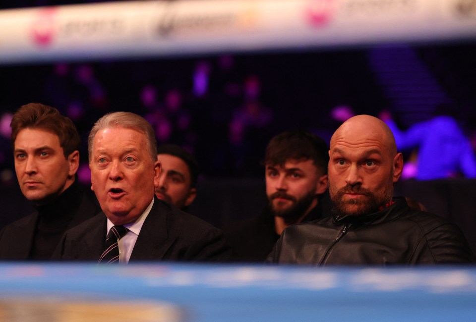 Tyson Fury and Frank Warren seated ringside at a boxing match.